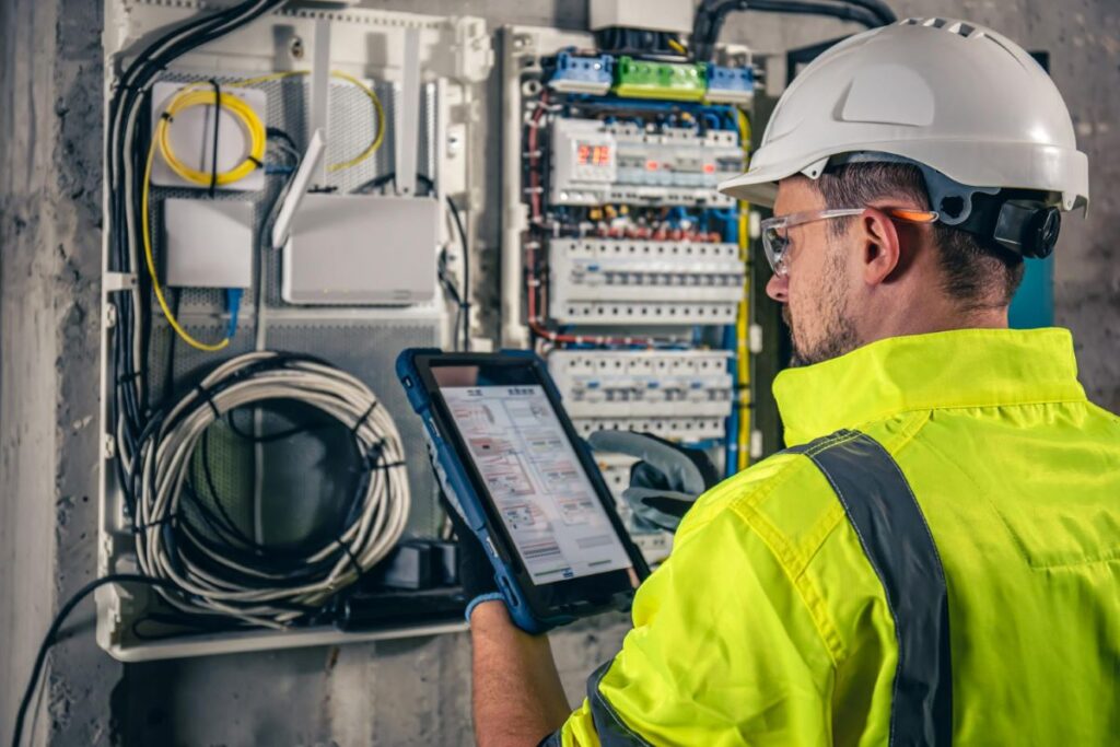 man electrical technician working switchboard with fuses uses tablet (2) energy code analysis inspection