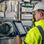 man electrical technician working switchboard with fuses uses tablet (2)